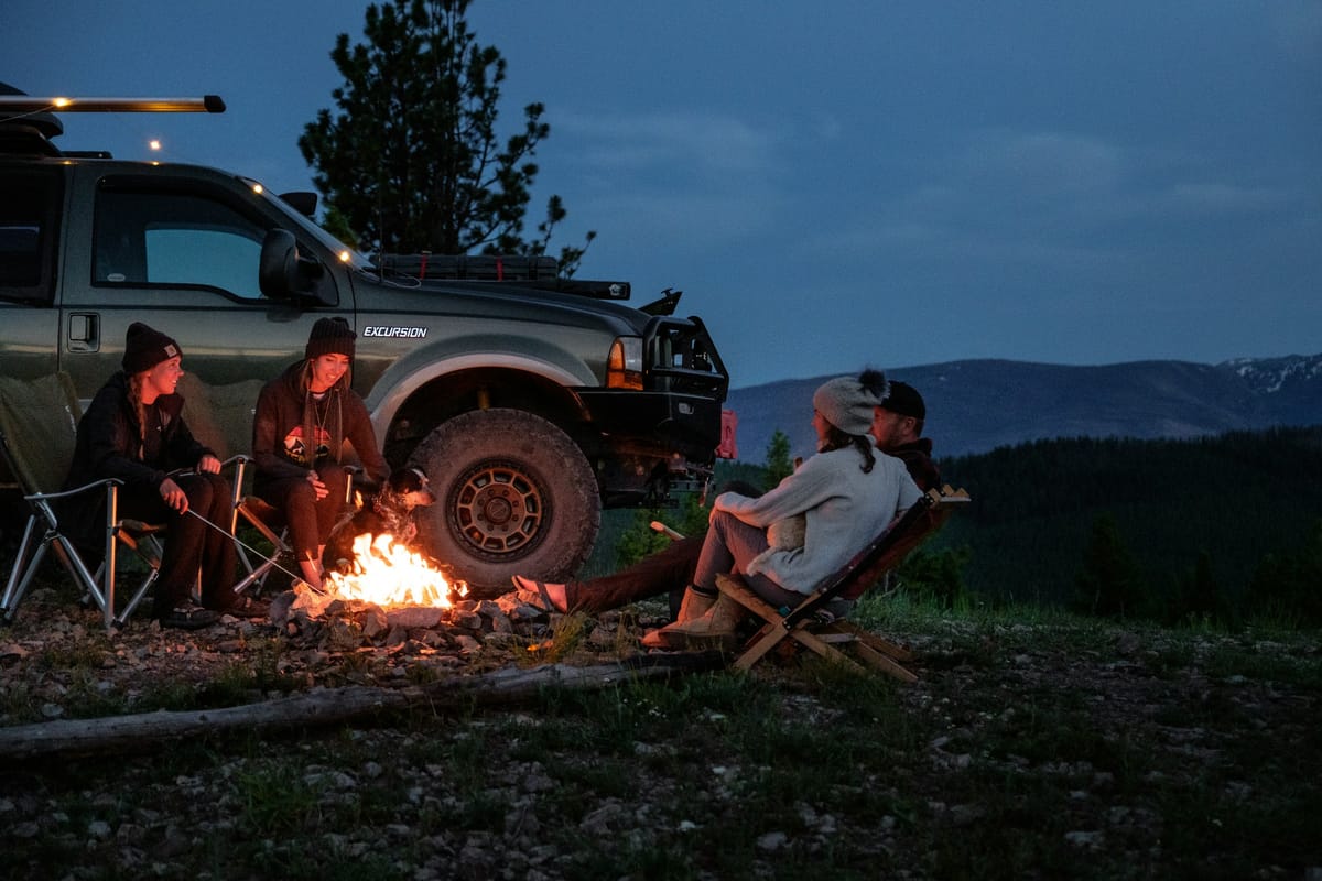 Campingstuehle und Feuer neben einem Fahrzeug in der Daemmerung